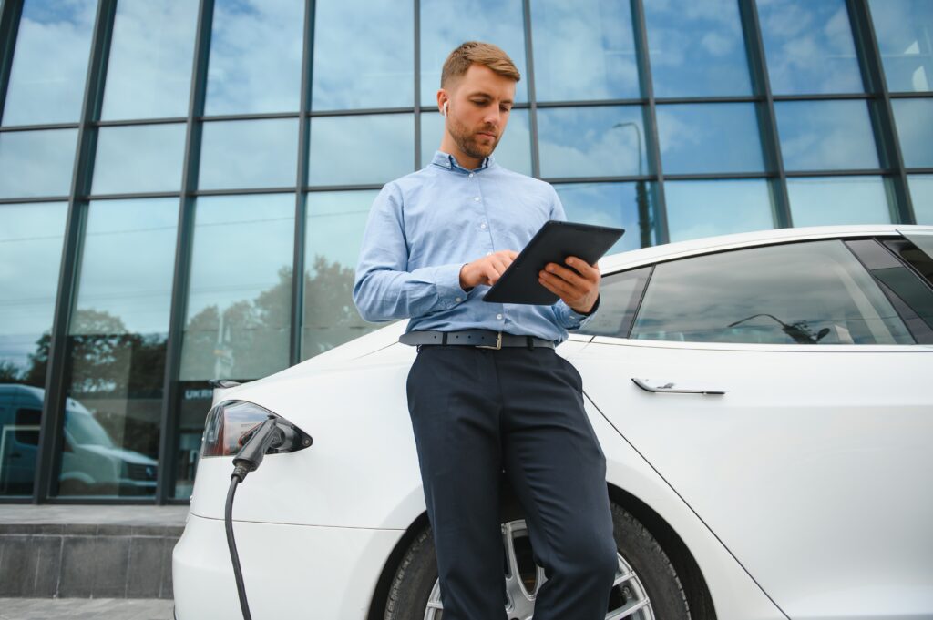 Zakelijke gebruiker bij laadpaal en elektrische auto met tablet – subsidieadvies over warmtepomp of warmtepompboiler via New Energy Systems