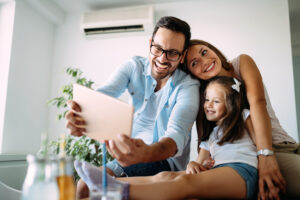 Gezin met jonge dochter kijkt lachend naar een tablet in een modern, licht huis met airco aan de muur